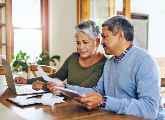 Senior couple, budget planning and health insurance checklist with computer at home. Documents, pension and elderly people with financial, tax and debt form in a house with bills and pc admin