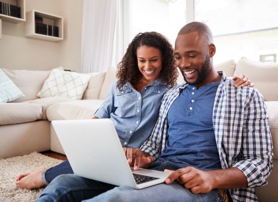 Young black couple using laptop sitting on the floor at home