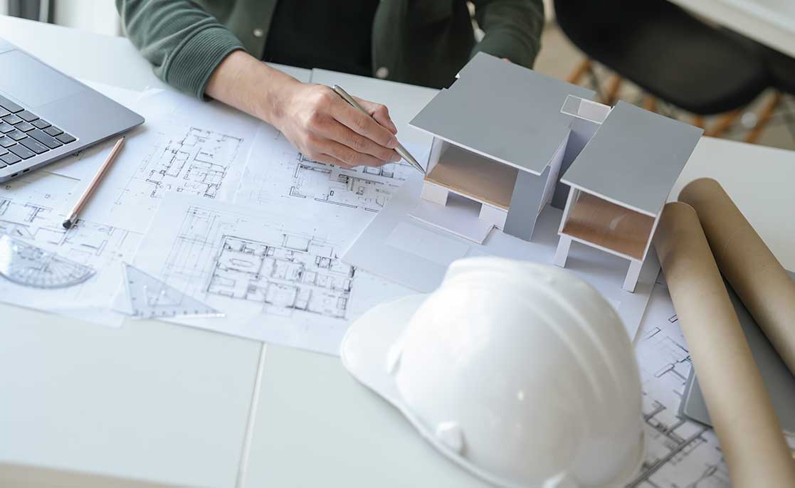 An individual in a hardhat uses a laptop to work on a project, emphasizing custom home building in McAllen.